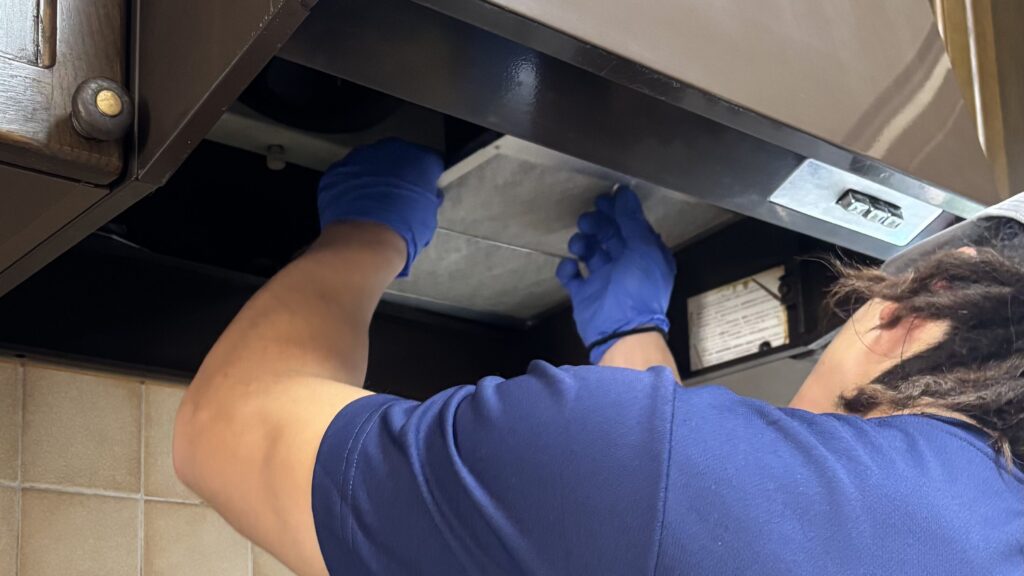 レンジフード内部の清掃・フィルター交換作業を行うハウスクリーニングスタッフの手元。